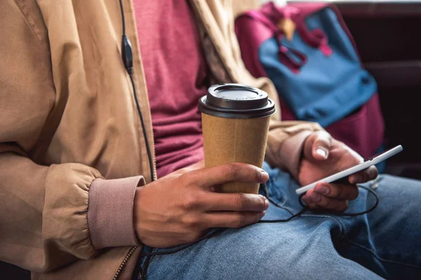 Cropped image of man with disposable coffee cup using smartphone during trip on travel bus — Stock Photo