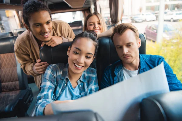 Amici multiculturali sorridenti guardando la mappa durante il viaggio in autobus di viaggio — Foto stock