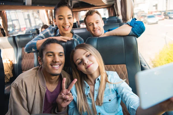 Young mixed race man doing peace sign with friends taking selfie on smartphone during trip on travel bus — Stock Photo