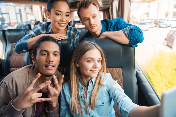Happy multiethnic friends taking selfie on smartphone during trip on travel bus — Stock Photo