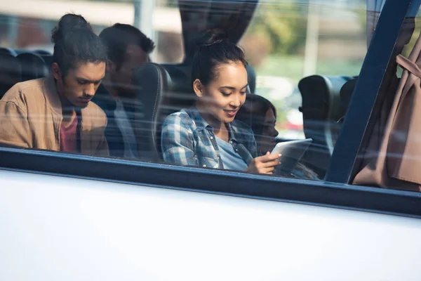 Красивая азиатская женщина с помощью цифрового планшета в то время как ее смешанной расы бойфренд сидит позади во время поездки на автобусе — стоковое фото