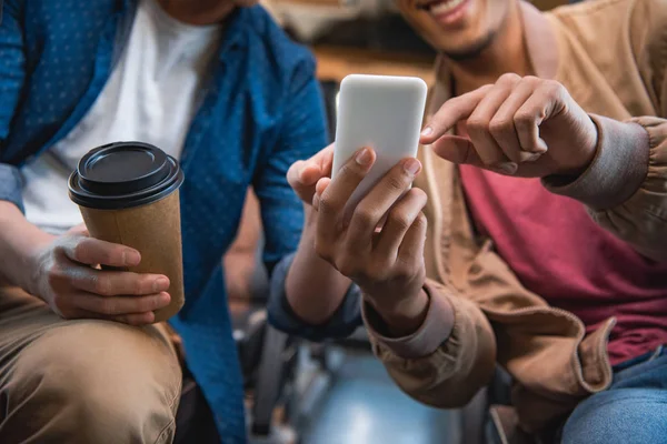 Imagem cortada do homem apontando para o smartphone para seu amigo masculino com xícara descartável de café durante a viagem em ônibus de viagem — Fotografia de Stock