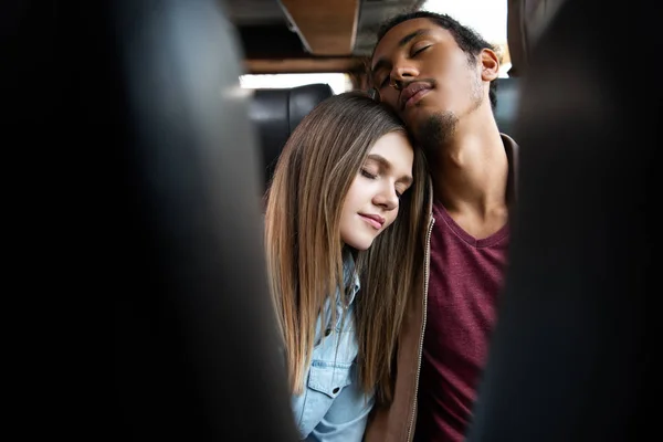 Enfoque selectivo de la joven pareja interracial durmiendo durante el viaje en autobús de viaje - foto de stock
