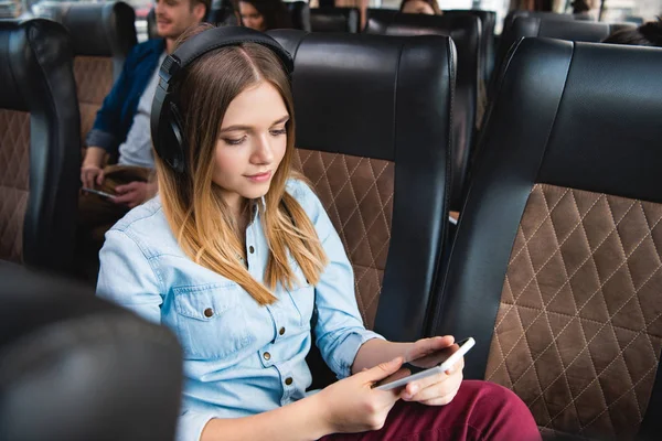 Junge Frau mit Kopfhörer hört Musik und nutzt Smartphone während Fahrt im Reisebus — Stockfoto