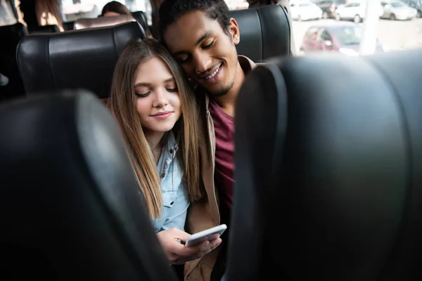 Beautiful young woman showing smartphone to her mixed race boyfriend during trip on bus — Stock Photo