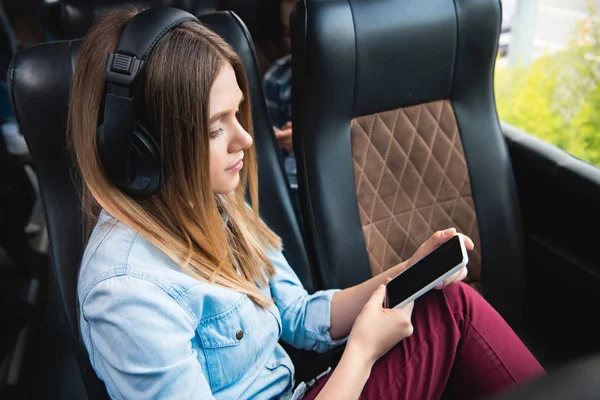 Selective focus of woman in headphones listening music and using smartphone during trip on travel bus — Stock Photo