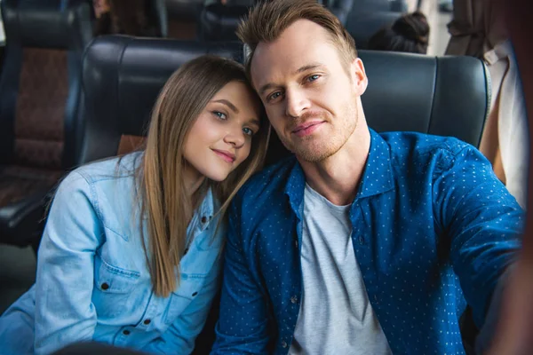 Cheerful man taking selfie with young girlfriend during trip on travel bus — Stock Photo