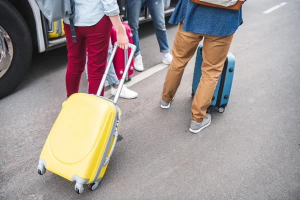 Vista parcial de los turistas con bolsas de ruedas cerca de autobús de viaje en la calle urbana - foto de stock