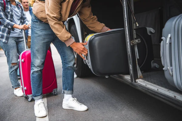 Image recadrée de l'homme mettant sac à roulettes dans le bus de voyage tandis que ses amis debout derrière à la rue — Photo de stock