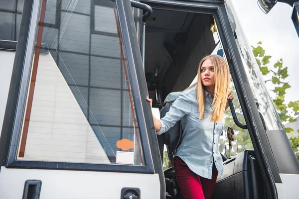 Foco seletivo de turista feminino com mochila olhando para fora de ônibus de viagem na rua urbana — Fotografia de Stock
