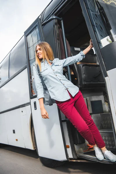 Vista de ángulo bajo del turista femenino con mochila posando cerca de autobús de viaje en la calle de la ciudad — Stock Photo