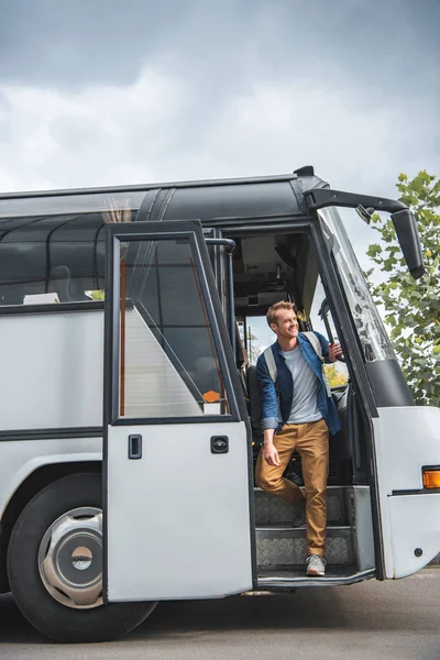 Happy male traveler with rucksack walking out from bus at city street — Stock Photo