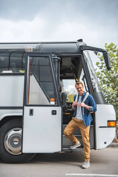 Homme souriant avec sac à dos posant près de bus de voyage à la rue urbaine — Photo de stock