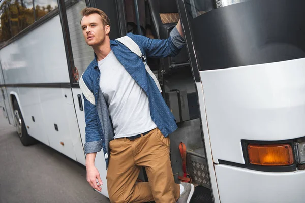 Handsome man with rucksack walking out from travel bus at urban street — Stock Photo