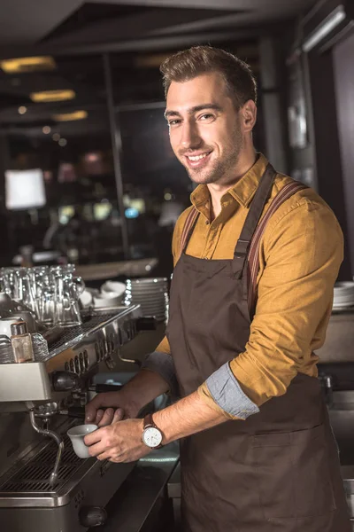 Handsome young barista preparing coffee with coffee machine in cafe and looking at camera — Stock Photo