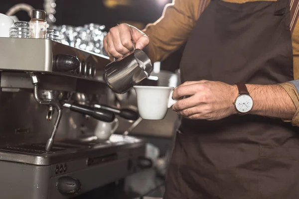 Tiro cortado de barista em avental derramando leite em café enquanto o prepara no restaurante — Fotografia de Stock