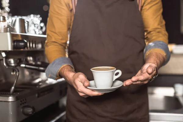 Tiro cortado de barista em avental segurando xícara de café feito fresco — Fotografia de Stock