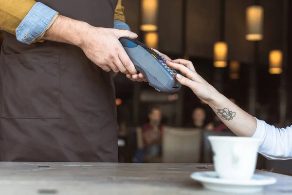 Corte tiro de garçom segurando terminal de pagamento enquanto o cliente entrar pino no café — Fotografia de Stock