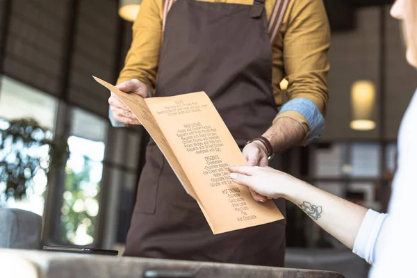 Corte tiro de garçom mostrando lista de menu para cliente feminino no café — Fotografia de Stock