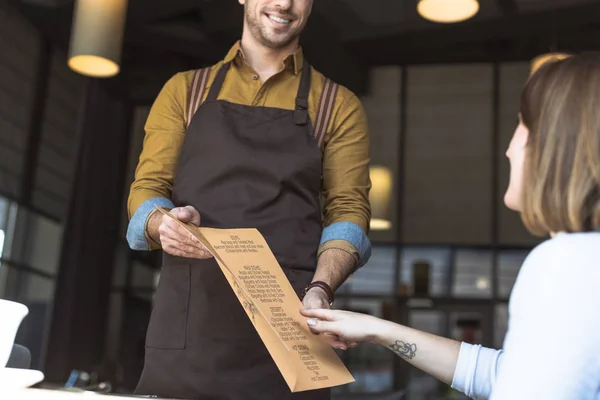 Plan recadré de serveur souriant montrant la liste des menus au client féminin dans le café — Photo de stock