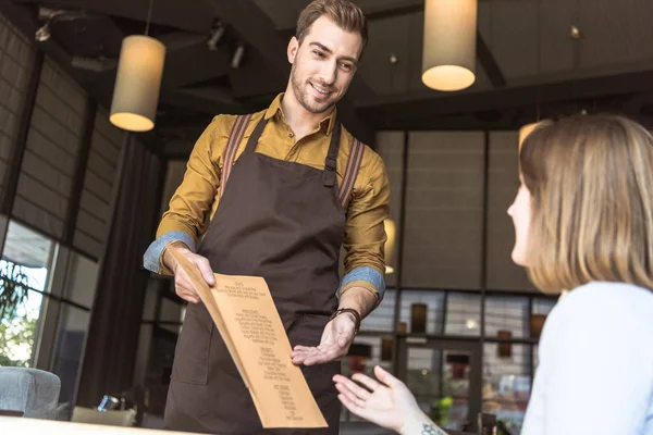 Felice giovane cameriere che mostra la lista dei menu al cliente femminile in caffè — Foto stock