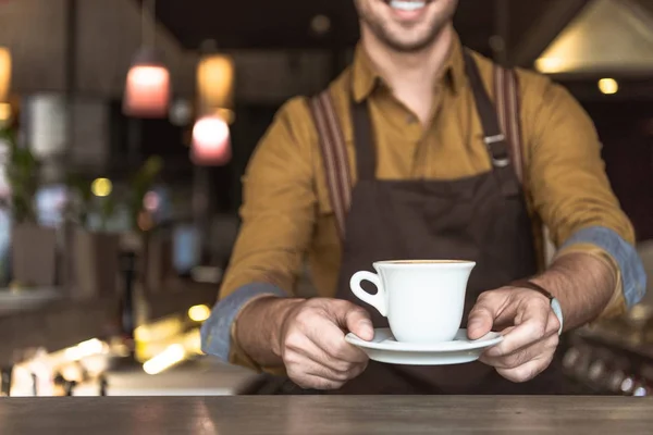 Tiro cortado de sorrir jovem barista segurando xícara de café — Fotografia de Stock