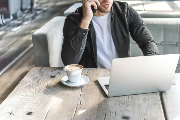 Plan recadré de jeune pigiste travaillant avec un ordinateur portable et parlant par téléphone au restaurant — Photo de stock