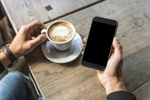 Recortado disparo de hombre con taza de cappuccino usando teléfono inteligente con pantalla en blanco - foto de stock