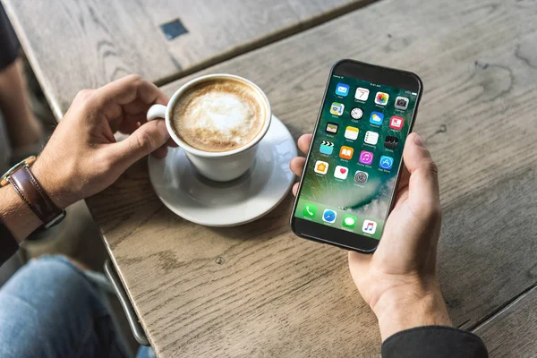 Tiro cortado do homem com xícara de cappuccino usando smartphone com tela inicial da maçã — Fotografia de Stock