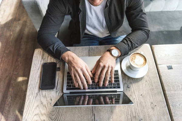 Vista de ángulo alto del joven freelancer que trabaja con el ordenador portátil en la cafetería - foto de stock