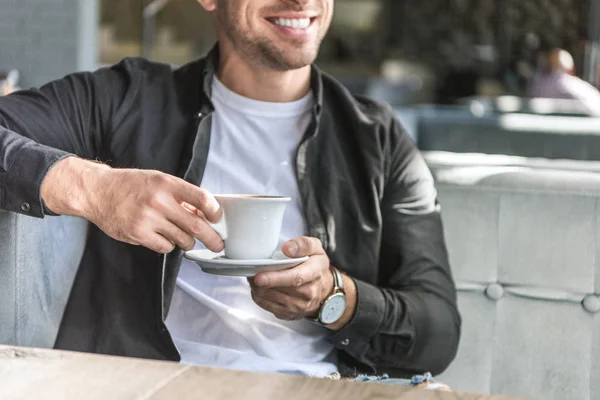 Recortado disparo de hombre joven con taza de café sentado en la cafetería - foto de stock