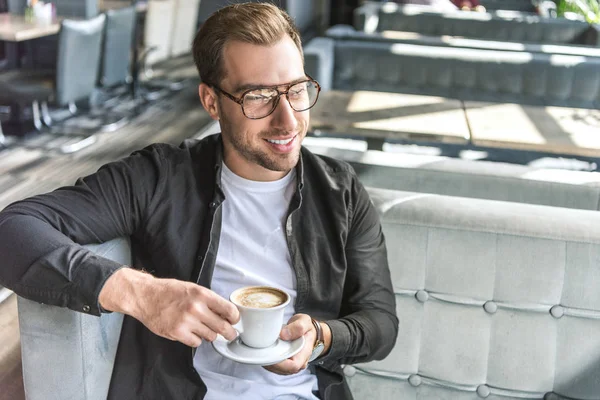 Joven guapo con taza de café sentado en la cafetería - foto de stock