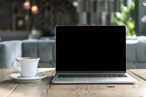 Xícara de café delicioso e laptop com tela em branco na mesa de madeira rústica no café — Fotografia de Stock