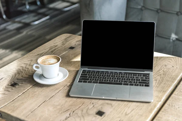 Tasse de café et ordinateur portable avec écran blanc sur table en bois rustique au café — Photo de stock