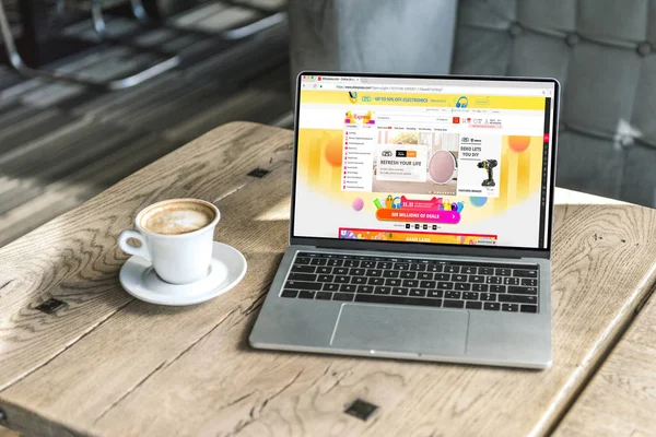 Taza de capuchino y portátil con sitio web aliexpress en la pantalla en la mesa de madera rústica en la cafetería - foto de stock