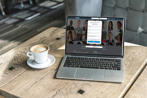 Чашка кофе и ноутбук с linkedin веб-сайт на экране на деревенском деревянный стол в кафе — стоковое фото