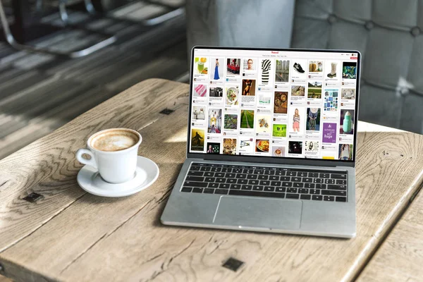 Xícara de café e laptop com site do pinterest na tela na mesa de madeira rústica no café — Fotografia de Stock