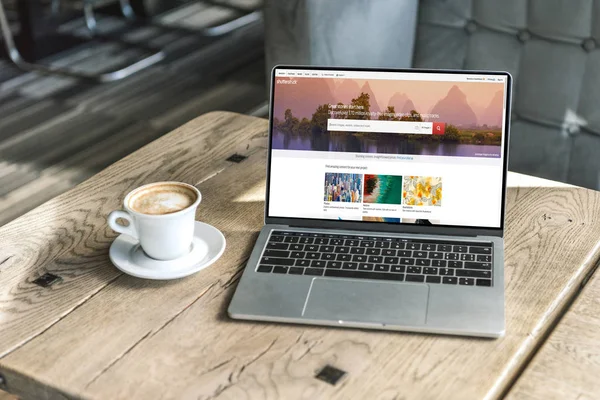Cup of coffee and laptop with shutterstock website on screen on wooden table at cafe — Stock Photo
