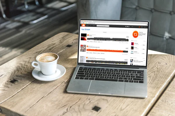 Cup of coffee and laptop with soundcloud website on screen on rustic wooden table at cafe — Stock Photo