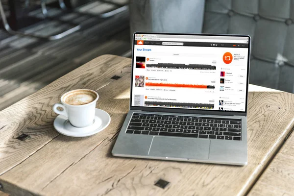Tasse Kaffee und Laptop mit Soundcloud-Website auf dem Bildschirm auf rustikalem Holztisch im Café — Stockfoto