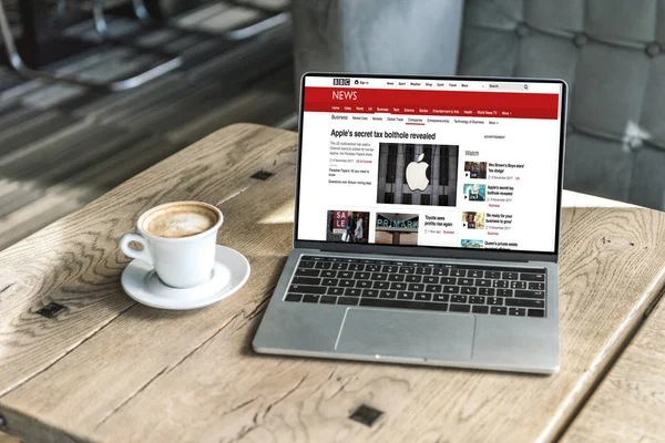 Cup of coffee and laptop with bbc website on screen on rustic wooden table at cafe — Stock Photo