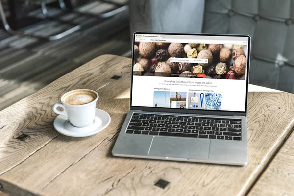 Taza de café y portátil con obturador sitio web en la pantalla en la mesa de madera en la cafetería - foto de stock