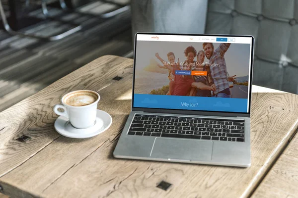 Cup of coffee and laptop with couchsurfing website on screen on rustic wooden table at cafe — Stock Photo