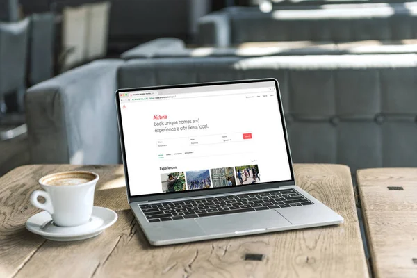 Tasse Kaffee und Laptop mit Airbnb-Webseite auf dem Bildschirm auf rustikalem Holztisch im Café — Stockfoto