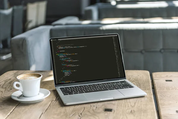 Tasse de café et ordinateur portable avec le code de programme à l'écran sur la table en bois rustique au café — Photo de stock