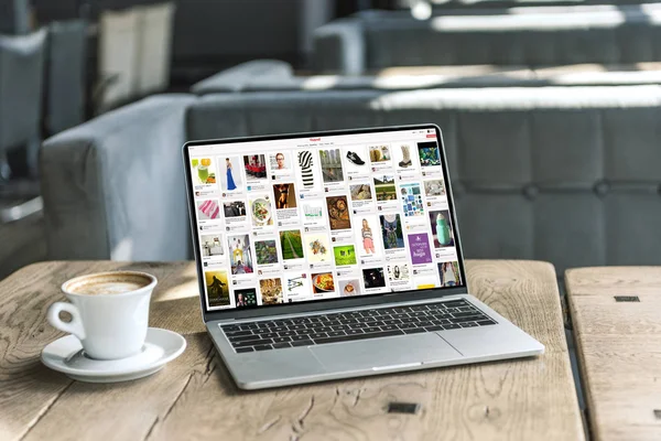 Taza de café y portátil con pinterest sitio web en la pantalla en la mesa de madera rústica en la cafetería - foto de stock