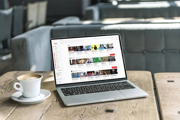 Tasse Kaffee und Laptop mit Youtube-Website auf dem Bildschirm auf rustikalem Holztisch im Café — Stockfoto