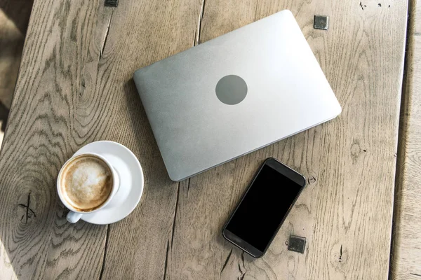 Vue du dessus de tasse de café avec smartphone et ordinateur portable sur table en bois rustique — Photo de stock