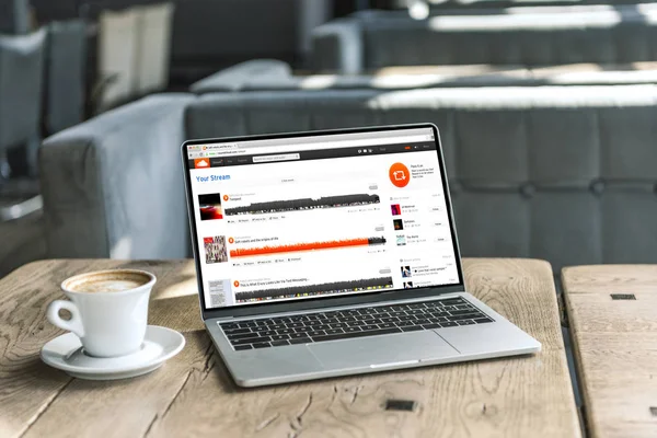 Cup of coffee and laptop with soundcloud website on screen on rustic wooden table at cafe — Stock Photo