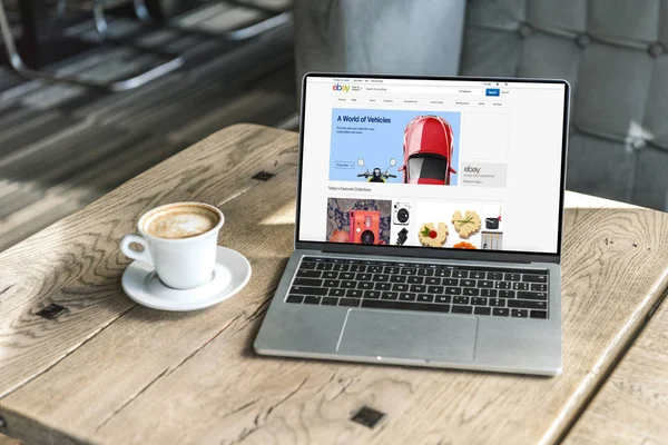 Cup of coffee and laptop with ebay website on screen on rustic wooden table at cafe — Stock Photo
